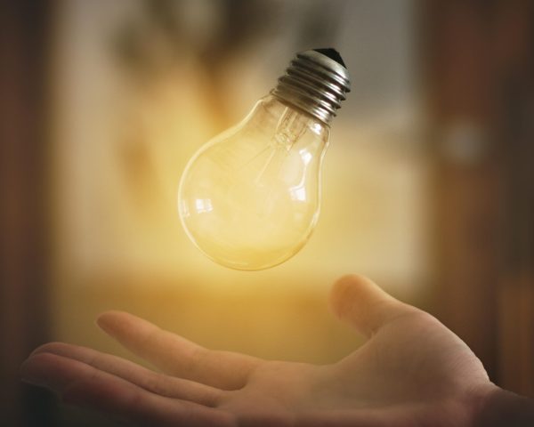 A glowing light bulb hovers above an open hand, symbolizing innovation and creativity.